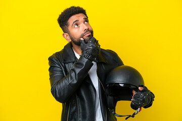 Young Brazilian man with a motorcycle helmet isolated on yellow background having doubts