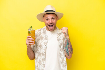 Young caucasian man holding a cocktail isolated on yellow background celebrating a victory in winner position