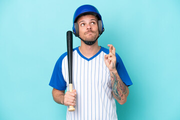 Baseball player with helmet and bat isolated on blue background with fingers crossing and wishing...