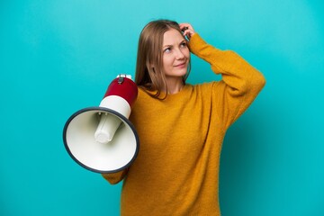 Young Russian woman isolated on blue background holding a megaphone and having doubts
