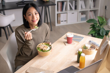 Asian woman eating healthy meal while working, Businesswoman having a lunch break at the office, Beautiful woman smiling and looking at camera while eating food