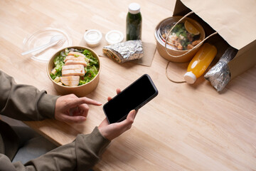 Asian woman eating healthy meal while working, Businesswoman having a lunch break at the office, hand holding phone with blank black screen for copyspace
