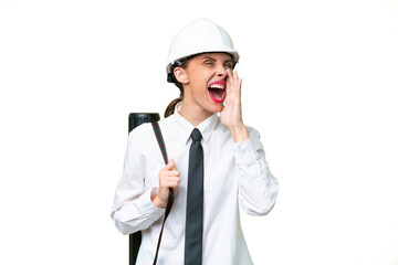 Young architect woman with helmet and holding blueprints over isolated background shouting with...