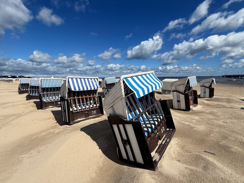coastal vibes on the beach, traditional wicker beach chairs (Strandkörbe) on golden sand by the sea, blue sky with fluffy white clouds