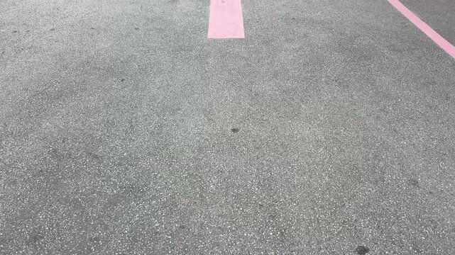 Pink arrow on cracked asphalt road surface indicating direction in urban setting
