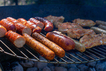 Grilled chicken pieces and sausages cooking over hot charcoal on an outdoor barbecue, with golden sear marks and a rustic metal grill.