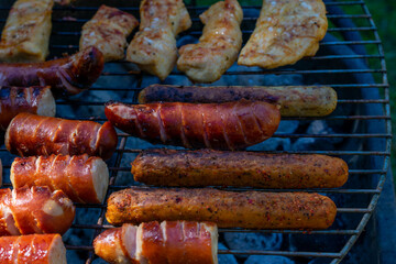 Fototapeta premium Grill loaded with sausages and marinated chicken, sizzling over hot charcoal, with smoke rising in the sunlight.