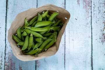 green pea pods in paper bag on rustic wooden table, top view