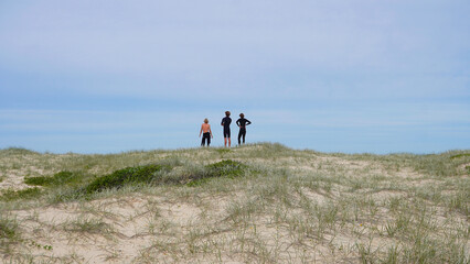 Surfers in Australia looking out at the ocean from behind.People standing on a sandy dune overlooking the ocean during a calm day at the beach