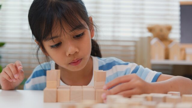 Young Asian girl focused on stacking wooden blocks, promoting STEM learning, creativity, and motor skill development. Concept of early education, problem solving, and cognitive growth.