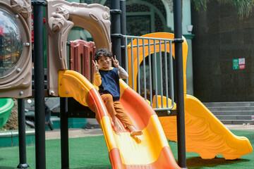 Happy child sliding down a colorful playground slide on a sunny day. Outdoor fun, childhood joy, and active play in a safe, urban recreational space.