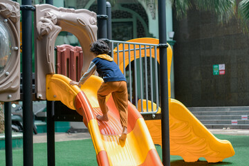 Happy child sliding down a colorful playground slide on a sunny day. Outdoor fun, childhood joy, and active play in a safe, urban recreational space.