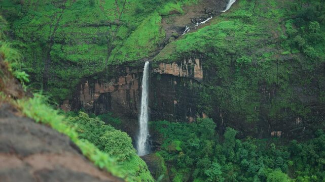 4K Slow motion shot of ring waterfall falling from a mountain cliff as seen from Savlya Ghat view point in Tamhini Ghat near Pune in Maharashtra, India during the monsoon season. Scenic waterfall view