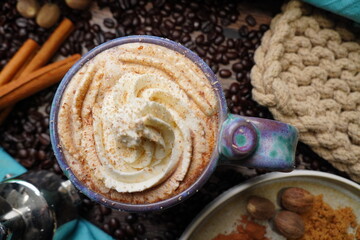 Cup or mug of coffee in a blue ceramic cup with whipped cream and a dash of nutmeg or cinnamon.  Coffee beans surrounding a cozy cup of coffee in a blue mug.  