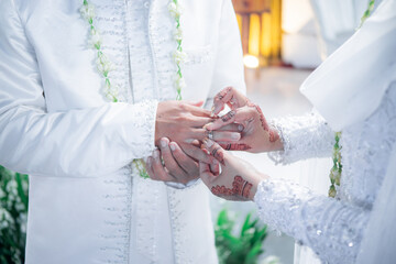 Bride and groom exchanging rings during a traditional Indonesian wedding ceremony, symbolizing their commitment and love. Asian muslim wedding