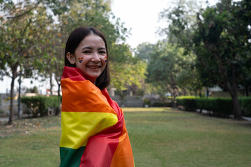 A joyful woman wrapped in a rainbow flag, celebrating diversity and inclusion in a vibrant outdoor...