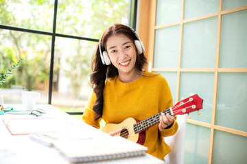 Young woman happy listen music for chill and playing guitar after finish work.   Lifestyle girl using laptop for meeting and working  in living room at home.  Lifestyle Concept