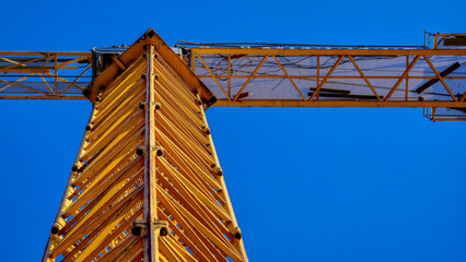 A yellow crane is standing tall against a blue sky. The crane is old and rusted, but it still stands strong. Concept of strength and resilience, as the crane has weathered the test of time