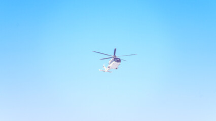 A helicopter is flying in the sky. The sky is blue and clear. The helicopter is white and black