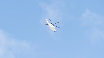 A white helicopter against a backdrop of a clear blue sky, a passenger helicopter in perfect visibility on a sunny day. A bird's-eye view of the landscape from above