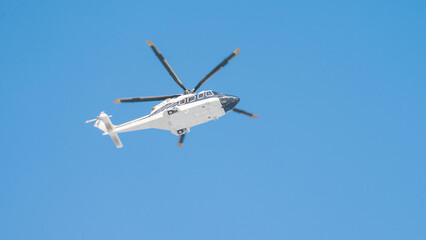 A white and black helicopter is flying in the sky. The helicopter is in the air and has a blue sky background