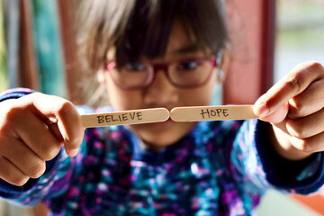 A little girl holds wooden sticks with “believe” and “hope”.