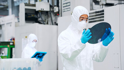 半導体工場でシリコンウエハーを検査する防塵服を着た男性作業員