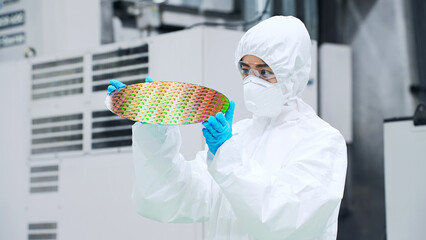 半導体工場でシリコンウエハーを検査する防塵服を着た女性作業員