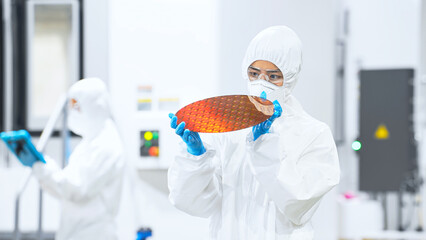 Naklejka premium 半導体工場でシリコンウエハーを検査する防護服を着た女性作業員
