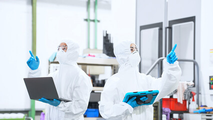 デジタルデバイスを持って工場で作業する防護服を着た男女作業員 © metamorworks