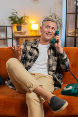 Happy Caucasian man with gray hair making wired telephone conversation with friends at home...
