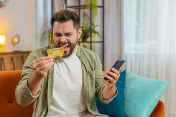 Angry stressed man trying to pay online shopping with smartphone blocked credit card. Annoyed...