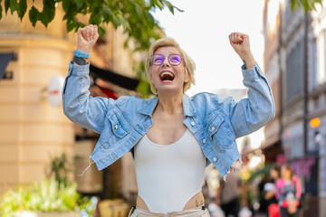 Excited surprised woman standing outdoors rejoices jumping with happiness feeling delight winning...