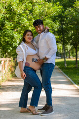 Fototapeta premium Happy pregnant woman with husband standing together in a sunny day in jeans and white shirt.