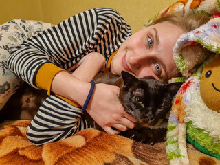 blonde girl lying on bed, holding big cat in hands, long hair, striped vest, smiling, teenager, soft toy avocado, vacation, relaxation, friends, family, pet, woman, beauty