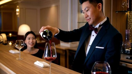 Elegant waiter in tuxedo pouring red wine at upscale bar, serving smiling guest in luxurious setting, symbolizing fine dining, hospitality, and premium service.