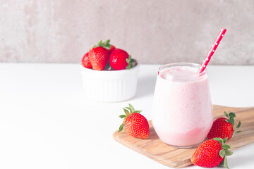 Glass of fresh strawberry milkshake, smoothie and fresh strawberries on white and wooden background. Healthy food and drink concept.