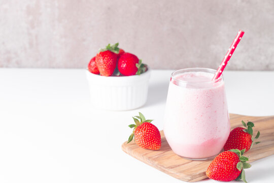 Glass of fresh strawberry milkshake, smoothie and fresh strawberries on white and wooden background. Healthy food and drink concept. - Powered by Adobe