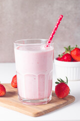 Glass of fresh strawberry milkshake, smoothie and fresh strawberries on white and wooden...