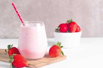 Glass of fresh strawberry milkshake, smoothie and fresh strawberries on white and wooden background. Healthy food and drink concept.