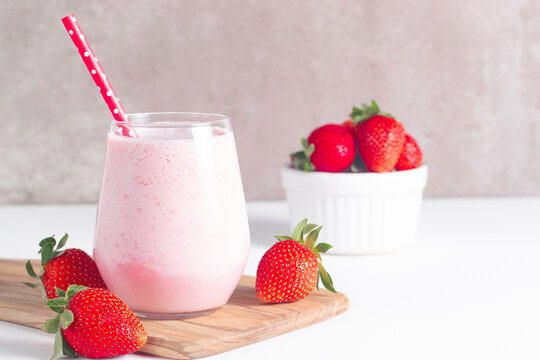 Glass of fresh strawberry milkshake, smoothie and fresh strawberries on white and wooden background. Healthy food and drink concept.