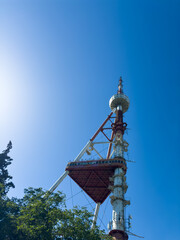 Old rusty red and white TV tower in Tbilisi against the background of blue sky and trees, vertical...