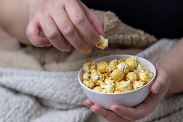 Close up asian woman hand relaxing with a bowl of sweet caramel popcorn. Perfect for cozy movie nights at home