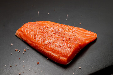Fresh raw salmon or trout fillet sprinkled with coarse salt. Black background. Healthy seafood food.