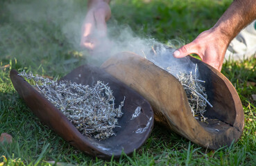 Australian Aboriginal smoking ceremony, human hands and wooden dish with a smoke of burning tree branches, the ritual rite at the community event, symbol of joining to the indigenous culture