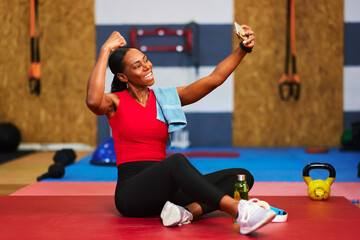 Fototapeta premium Smiling sportswoman taking selfie after successful workout at the gym