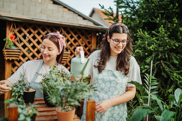 Two female friends or sisters taking care of plants with water can and mister