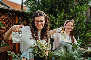 Two female friends or sisters taking care of plants with water can and mister