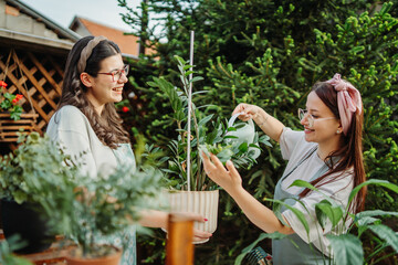 Two female friends or sisters taking care of plants with water can and mister