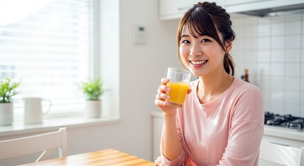 Smiling Asian woman in her kitchen enjoys a glass of orange juice at the table, bright and cheerful, wellness and health, a refreshing morning.
